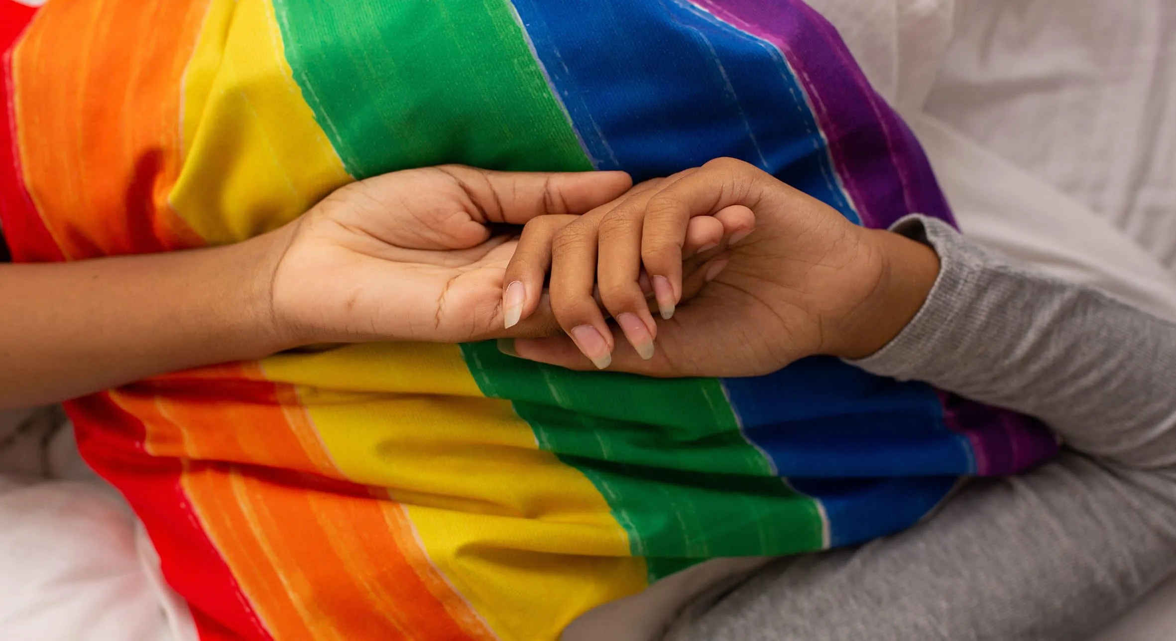 Queer Kentucky hero image of two females holding hands on rainbow flag